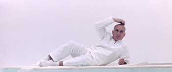 Movie still from “THX 1138” (1971), directed by George Lucas – A man laying on the ground wearing all white clothes; Medium shot, Low angle