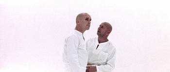 Movie still from “THX 1138” (1971), directed by George Lucas – Two bald men in white shirts looking at each other; Medium shot, Low angle