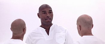 Movie still from “THX 1138” (1971), directed by George Lucas – A man in a white shirt is posing for a picture; Close Up shot, Low angle