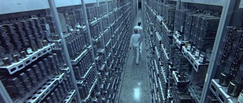 Movie still from “THX 1138” (1971), directed by George Lucas – Two men walking down a long hallway in front of a bunch of racks of computer equipment; Extreme Wide shot, High angle