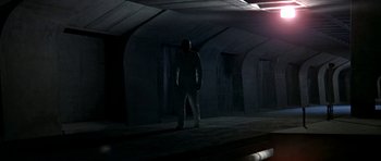 Movie still from “THX 1138” (1971), directed by George Lucas – A man standing in the dark in a building; Wide shot, Low angle