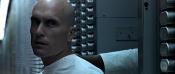 Movie still from “THX 1138” (1971), directed by George Lucas – A man with bald head sitting next to a wall; Close Up shot, Low angle