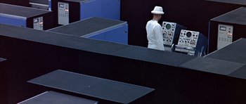 Movie still from “THX 1138” (1971), directed by George Lucas – A man wearing a white hat standing next to a black counter; Extreme Wide shot, High angle