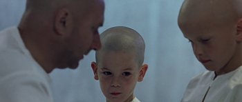 Movie still from “THX 1138” (1971), directed by George Lucas – A young boy with a shaved head looking at a bald man; Close Up shot, Over the shoulder angle