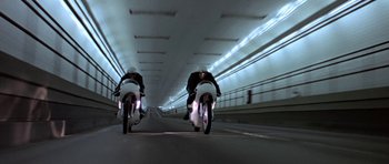 Movie still from “THX 1138” (1971), directed by George Lucas – Two people on motorcycles riding down a tunnel; Wide shot, Low angle