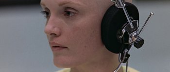 Movie still from “THX 1138” (1971), directed by George Lucas – A woman wearing a pair of headphones and looking to her left; Close Up shot, Overhead angle