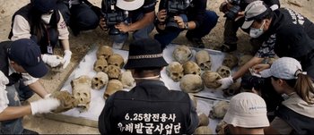 Movie still from “Tae Guk Gi: The Brotherhood of War” (2004), directed by Kang Je-kyu – A group of people standing around a pile of skulls; Medium shot, High angle