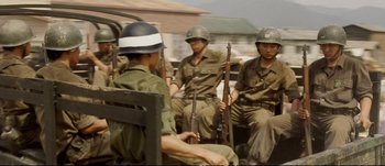 Movie still from “Tae Guk Gi: The Brotherhood of War” (2004), directed by Kang Je-kyu – A group of men sitting next to each other holding guns; Medium shot, Over the shoulder angle