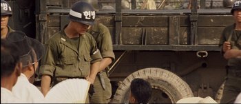 Movie still from “Tae Guk Gi: The Brotherhood of War” (2004), directed by Kang Je-kyu – A man in a military uniform standing next to a truck; Medium shot, Over the shoulder angle
