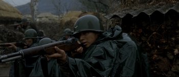 Movie still from “Tae Guk Gi: The Brotherhood of War” (2004), directed by Kang Je-kyu – A man wearing a helmet and holding a rifle in his hand; Close Up shot, Low angle