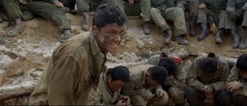 Movie still from “Tae Guk Gi: The Brotherhood of War” (2004), directed by Kang Je-kyu – A group of men sitting on the ground with mud on their faces; Medium shot, High angle