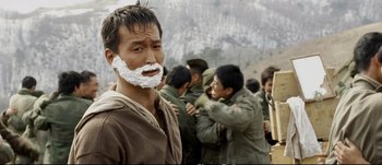 Movie still from “Tae Guk Gi: The Brotherhood of War” (2004), directed by Kang Je-kyu – A group of people gathered around a man with shaving cream on his face; Close Up shot, Over the shoulder angle