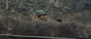 Movie still from “Tae Guk Gi: The Brotherhood of War” (2004), directed by Kang Je-kyu – A man in a helmet is holding a rifle in his hand; Medium shot, High angle