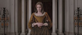 Movie still from “Tale of Tales” (2015), directed by Matteo Garrone – A woman dressed in medieval clothing sitting in front of pillars; Medium shot, Low angle