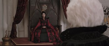 Movie still from “Tale of Tales” (2015), directed by Matteo Garrone – A woman sitting on top of a chair wearing a red and black dress; Wide shot, Over the shoulder angle