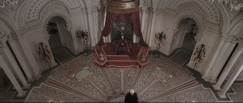 Movie still from “Tale of Tales” (2015), directed by Matteo Garrone – A man sitting on top of a red couch in an ornate room; Extreme Wide shot, High angle