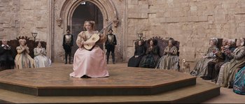 Movie still from “Tale of Tales” (2015), directed by Matteo Garrone – A group of people sitting on a stage with a woman holding a guitar; Wide shot, High angle