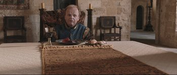 Movie still from “Tale of Tales” (2015), directed by Matteo Garrone – A man sitting at a table with a plate of food in front of him; Medium shot, High angle
