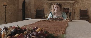 Movie still from “Tale of Tales” (2015), directed by Matteo Garrone – A woman sitting at a table with a glass of red wine; Medium shot, Over the shoulder angle