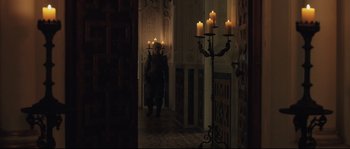 Movie still from “Tale of Tales” (2015), directed by Matteo Garrone – A man standing in front of candles in a dark room; Wide shot, Over the shoulder angle