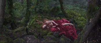 Movie still from “Tale of Tales” (2015), directed by Matteo Garrone – A woman in a red dress laying on the ground in the woods; Wide shot, Overhead angle