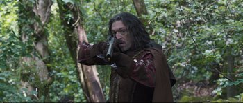 Movie still from “Tale of Tales” (2015), directed by Matteo Garrone – A man with long black hair holding a gun in the woods; Medium shot, Over the shoulder angle