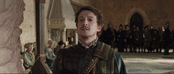 Movie still from “Tale of Tales” (2015), directed by Matteo Garrone – A man with a beard and a chain around his neck; Medium shot, Over the shoulder angle