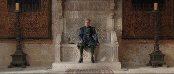 Movie still from “Tale of Tales” (2015), directed by Matteo Garrone – A man sitting on top of an ornate stone bench; Wide shot, Low angle