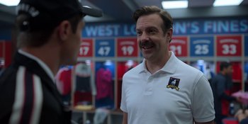 Movie still from “Ted Lasso” (2020), created by Brendan Hunt – A man in a white shirt talking to another man in a white shirt; Medium shot, Over the shoulder angle