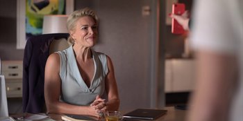 Movie still from “Ted Lasso” (2020), created by Brendan Hunt – A woman sitting at a table with a glass of water; Medium shot, Over the shoulder angle