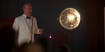 Movie still from “Ted Lasso” (2020), created by Brendan Hunt – An older man in a tuxedo is speaking to a crowd; Medium shot, Over the shoulder angle