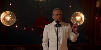 Movie still from “Ted Lasso” (2020), created by Brendan Hunt – A man in a white suit is holding a microphone; Medium shot, Over the shoulder angle