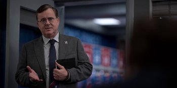 Movie still from “Ted Lasso” (2020), created by Brendan Hunt – A man in a suit and tie holding a book in his hand; Close Up shot, Over the shoulder angle