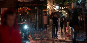 Movie still from “Ted Lasso” (2020), created by Brendan Hunt – A woman holding an umbrella while standing in the rain; Wide shot, Low angle