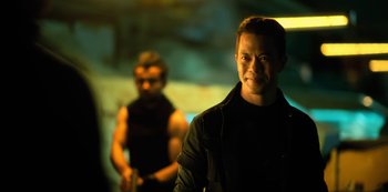 Movie still from “Altered Carbon” (2018), created by Laeta Kalogridis – A man standing next to another man in a dark room; Medium shot, Over the shoulder angle