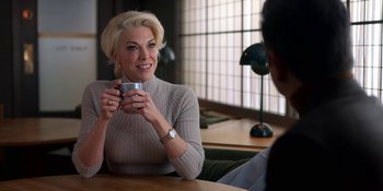 Movie still from “Ted Lasso” (2020), created by Brendan Hunt – A woman sitting at a table holding a coffee mug; Close Up shot, Over the shoulder angle