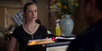 Movie still from “Ted Lasso” (2020), created by Brendan Hunt – A woman sitting in front of a table with a vase of flowers; Close Up shot, Over the shoulder angle