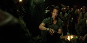 Movie still from “Altered Carbon” (2018), created by Laeta Kalogridis – A man sitting on the ground in front of a tree; Medium shot, Over the shoulder angle