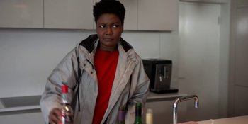 Movie still from “Ted Lasso” (2020), created by Brendan Hunt – A woman standing in a kitchen with a bottle of wine; Medium shot, Over the shoulder angle