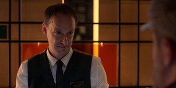 Movie still from “Ted Lasso” (2020), created by Brendan Hunt – A man in a vest and tie standing in front of a window; Close Up shot, Over the shoulder angle