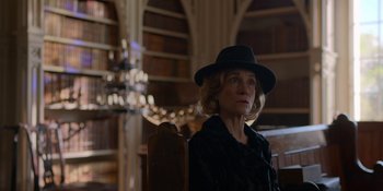 Movie still from “Ted Lasso” (2020), created by Brendan Hunt – An older woman wearing a black hat in a library; Medium shot, Low angle