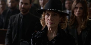 Movie still from “Ted Lasso” (2020), created by Brendan Hunt – An older woman wearing a black hat in front of a group of people; Close Up shot, Over the shoulder angle