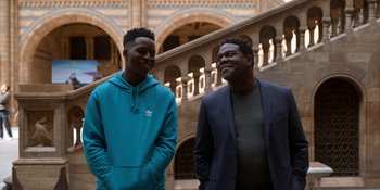 Movie still from “Ted Lasso” (2020), created by Brendan Hunt – Two men standing next to each other in front of a building; Medium shot, Low angle