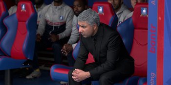 Movie still from “Ted Lasso” (2020), created by Brendan Hunt – A man in a suit sitting in a chair with other men; Medium shot, High angle