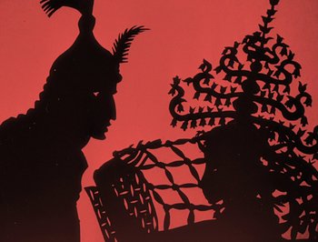 Movie still from “The Adventures of Prince Achmed” (1926), directed by Lotte Reiniger – A silhouette of a man and a woman sitting on a chair; Medium shot, Overhead angle