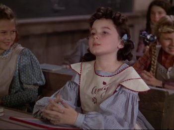 Movie still from “The Adventures of Tom Sawyer” (1938), directed by Norman Taurog – A young girl sitting at a table with her hands clasped together; Medium shot, High angle