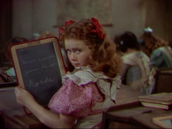 Movie still from “The Adventures of Tom Sawyer” (1938), directed by Norman Taurog – A little girl holding a chalkboard in a classroom; Medium shot, High angle