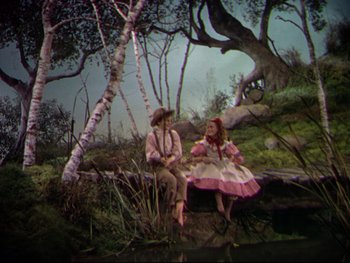 Movie still from “The Adventures of Tom Sawyer” (1938), directed by Norman Taurog – Two people sitting on a bench near a body of water; Wide shot, High angle