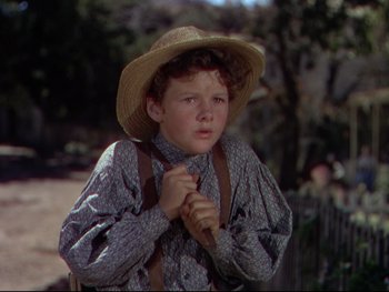 Movie still from “The Adventures of Tom Sawyer” (1938), directed by Norman Taurog – A young boy wearing a straw hat and holding a tie; Medium shot, High angle