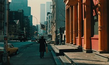 Movie still from “The American Friend” (1977), directed by Wim Wenders – A person walking down a street with a bag; Wide shot, Low angle